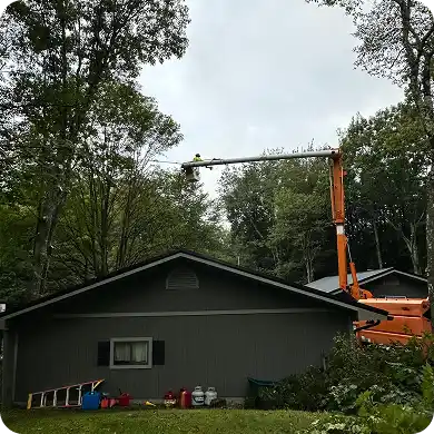 Arborist in an orange bucket truck trimming trees over the roof of a house.