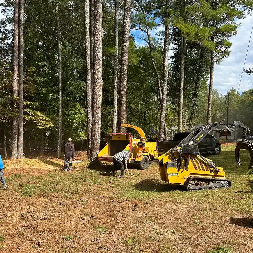 Tree service crew clearing a lot with a wood chipper and heavy equipment.